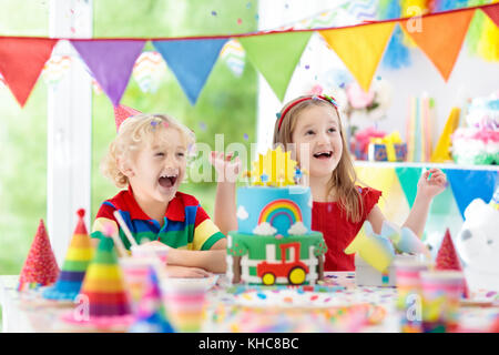 Kids Birthday party. child blowing out candles on cake coloré. Décoration maison avec des bannières drapeau arc-en-ciel, des ballons, des confettis et de les transporter à la ferme. Banque D'Images