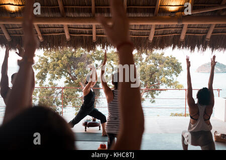 Groupe de plusieurs personnes pratiquant le yoga sur une terrasse palapa. yoga retreat Puerto Vallarta, Mexique - mismaloya Banque D'Images