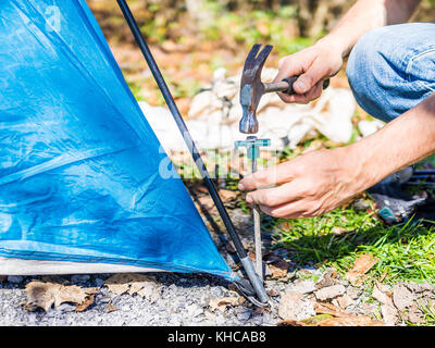 Jeune homme établir le campement de tentes de camping voyage de camping en martelant clouer au sol avec un marteau sur le coin Banque D'Images