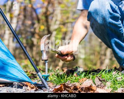 Jeune homme établir le campement de tentes de camping voyage de camping en martelant clouer au sol avec un marteau sur le coin Banque D'Images