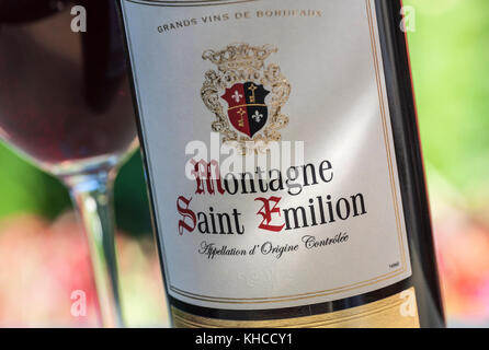 Montagne Saint Emilion vin ensoleillée avec étiquettes pour bouteilles de vin rouge derrière le verre de dégustation de vin floral en situation d'alfresco Banque D'Images