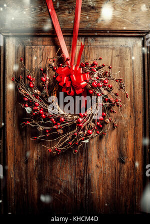 Couronne de Noël fait main accroché sur de vieilles portes en bois avec ruban rouge et de baies avec de la neige, vue de face Banque D'Images