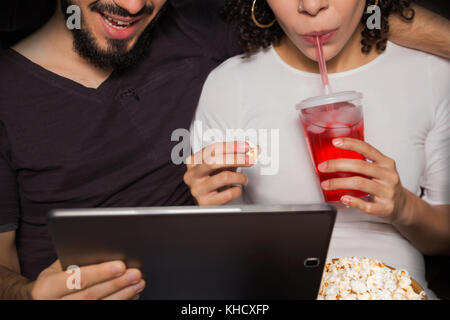 Sweet couple est regardant la vidéo sur tablette numérique. Ils sont eating popcorn et boisson. close up, sans visage. focus sélectif. eating popcorn et d