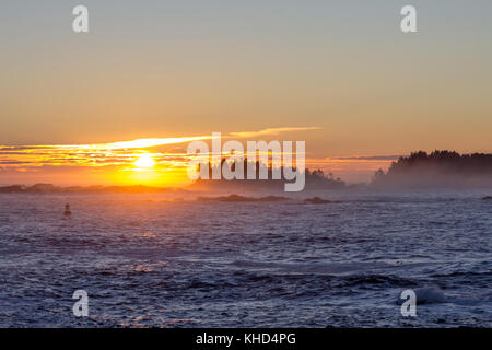 Grand soleil se lève à l'horizon d'une lueur orange et l'éclairage de fond de l'archipel Broken Group sur l'ouest sauvage de l'île de Vancouver Banque D'Images