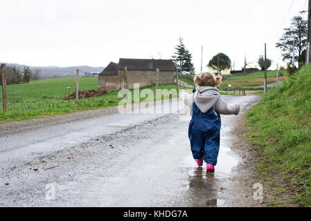Petite fille qui marche le long chemin de terre humide Banque D'Images