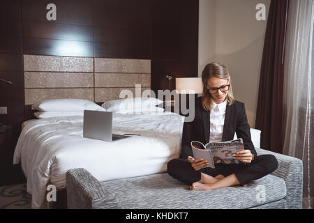 Businesswoman reading magazine dans l'hôtel Banque D'Images