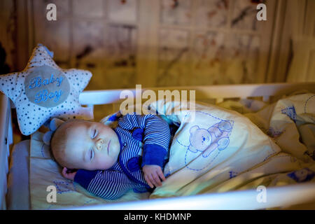 Adorable bébé nouveau-né garçon, dormant dans un lit bébé dans la nuit. Petit garçon au pyjama rayé bleu faire la sieste dans une pièce sombre, la décoration de Noël dans la chambre, Banque D'Images