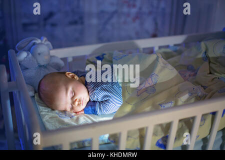 Adorable bébé nouveau-né garçon, dormant dans un lit bébé dans la nuit. Petit garçon au pyjama rayé bleu faire la sieste dans une pièce sombre, la décoration de Noël dans la chambre, Banque D'Images