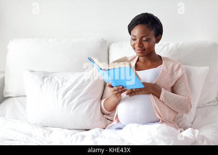 Happy pregnant african woman reading book at home Banque D'Images