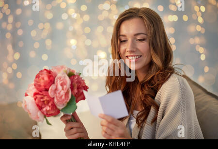 Femme heureuse avec des fleurs et carte de souhaits à la maison Banque D'Images