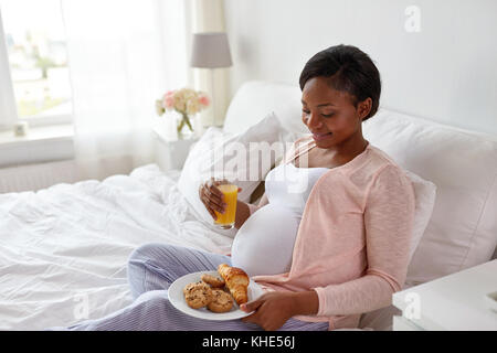 Femme enceinte avec du jus d'orange et pâtisseries au lit Banque D'Images