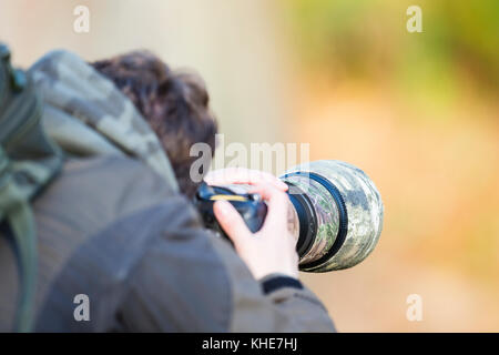 Richmond Park, Londres. Un photographe masculin à l'aide d'une caméra avec un grand objectif camouflé prend une photo. Banque D'Images