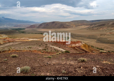Vue panoramique sur le dessus d'un paysage désertique avec des montagnes multicolores, des fissures dans le sol et la végétation est clairsemée sur le fond de ciel nuageux Banque D'Images