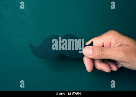 Libre de la main d'un young caucasian man holding a fake moustache sur fond vert Banque D'Images