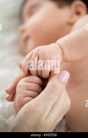 Bébé endormi tenant le doigt de maman. La maternité et l'enfance concept.