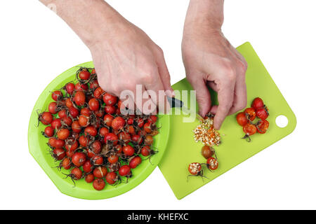 L'usinage avec couteau et mains de baies rouges de médicinales vitamine forest dogroseberries. retrait de figues de graines avec un couteau. Vue de dessus isolé Banque D'Images