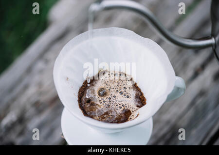 Délicieux café pourover épanouissement tandis que l'homme verse de l'eau dans le goutteur sur le terrain les grains de café. pique-nique estival sur la vieille table en bois backgrou Banque D'Images