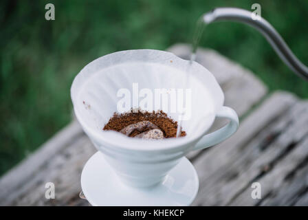 Délicieux café pourover épanouissement tandis que l'homme verse de l'eau dans le goutteur sur le terrain les grains de café. pique-nique estival sur la vieille table en bois backgrou Banque D'Images