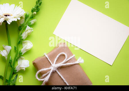 Idée de carte de vœux avec une note papier entouré de fleurs blanches et d'une boîte cadeau enveloppé dans du papier brun et attaché avec une chaîne de lin et Bow, sur un green b Banque D'Images