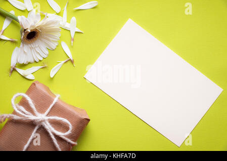 Thème communication image avec un papier vierge remarque, une fleur de chrysanthème blanc déchiré et une boîte-cadeau enveloppé dans du papier brun vintage, sur un papier jaune Banque D'Images
