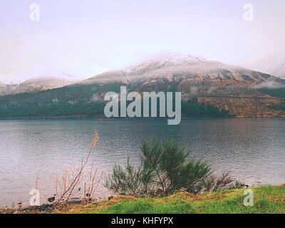 Lac de montagne avant le coucher du soleil à misty higland en Ecosse. Cône de neige de montagne au-dessus du niveau de l'eau. mise en miroir de l'herbe sèche et Heather buissons sur les banques Banque D'Images