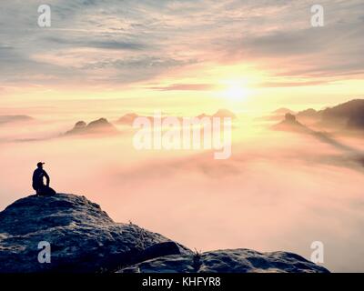 Moment de solitude sur le sommet rocheux exposés. man in black profitez d'une vue merveilleuse. s'asseoir sur le randonneur pic de roche et de regarder dans la brume et le brouillard coloré Banque D'Images