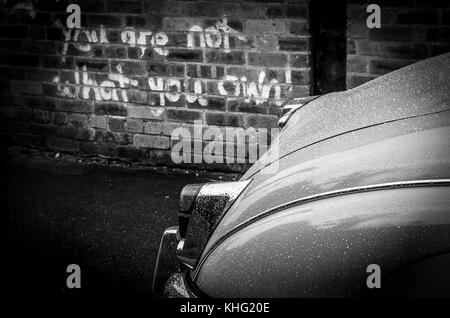 Jaguar Mk2 garé dans une scène industrielle avec graffiti écrit sur le wal citant 'VOUS N'ÊTES PAS CE QUE VOUS PROPRE' La photo est à l'arrière sur blanc comme Morse Banque D'Images