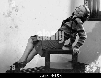2139795 Jeune femme portant une jupe et cardigan à rayures, couchée sur une chaise pour un studio portrait, 1940-1950 Banque D'Images