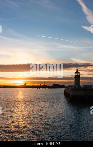 Coucher de soleil sur The Pegwell Bay lointain vu de Ramsgate Harbour avec phare sur fin de mur du port. Ciel Orange sur horizon tournant au bleu, quelques nuages. Banque D'Images