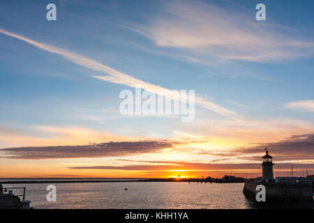 Coucher de soleil sur The Pegwell Bay lointain vu de Ramsgate Harbour avec phare sur fin de mur du port. Ciel Orange sur horizon tournant au bleu, quelques nuages. Banque D'Images