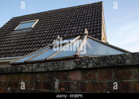 Vue sur un grand mur de briques rouges sur un toit de maison et serre ou maison d'été en verre derrière. Banque D'Images