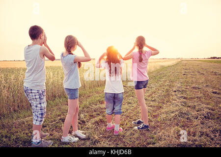 Quatre jeunes enfants caucasiens debout à été ensoleillé dans le champ Distance. Ils portent des vêtements d'été occasionnels et baskets. Banque D'Images