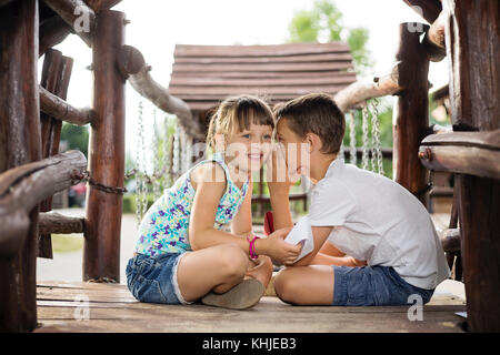 Deux frères de race blanche sittign heureux dans une maison en bois en plein air, sur la tenue d'un jour d'été, bateaux de papier dans les mains, boy whispering a secret en rif Banque D'Images