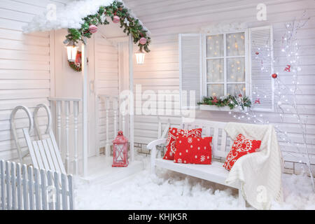 Extérieur d'hiver d'une maison de campagne avec des décorations de Noël dans le style américain. cour couverte de neige avec un porche, arbre, banc en bois blanc et Banque D'Images