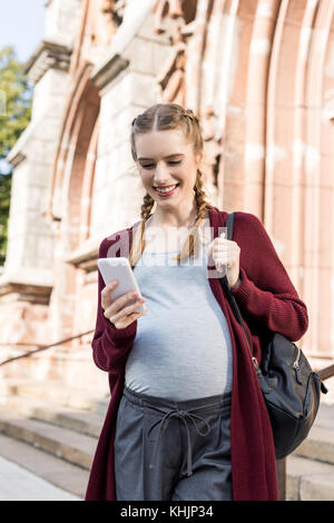 Portrait of smiling pregnant woman using smartphone sur street Banque D'Images