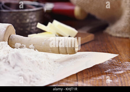 Ancienne en bois rouleau à pâtisserie saupoudrée de farine blanche sur une table rustique. beurre et tasses à mesurer en arrière-plan. faible profondeur de champ avec foc sélective Banque D'Images