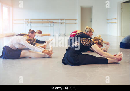 Vue latérale du ballet danse femmes méconnaissables assis sur le plancher et la flexion tout en faisant de la gymnastique dans la classe. Banque D'Images