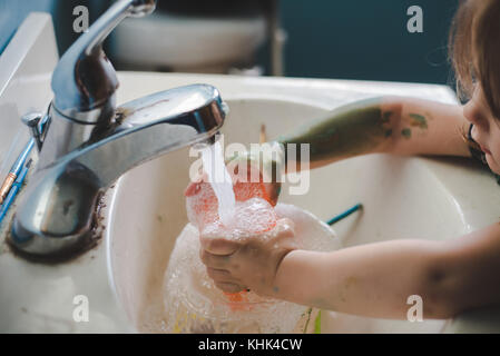 Un bébé fille lave la peinture sur ses mains dans un évier de salle de bains. Banque D'Images