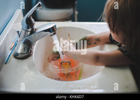 Un bébé fille lave la peinture sur ses mains dans un évier de salle de bains. Banque D'Images