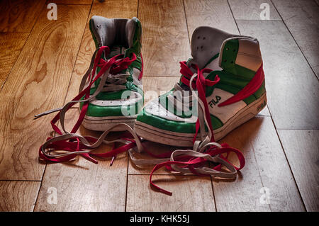 Chaussures Fila (baskets) bien portées et qui commencent à montrer leur âge avec des lacets de couleur. Il était assis sur un parquet. Banque D'Images