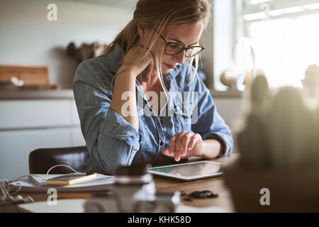 L'accent jeunes femme entrepreneur travaillant sur sa petite entreprise avec une tablette numérique tout en restant assis à sa table de cuisine à la maison Banque D'Images