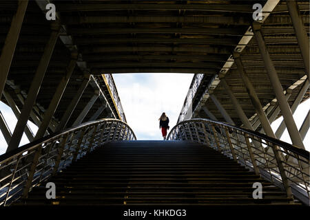 Vue symétrique d'une passerelle avec une femme qui monte les escaliers vus de derrière. Banque D'Images