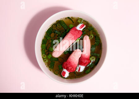 Les doigts d'un bouillon de viande avec des oignons verts flottant à la surface de la soupe dans un bol rose. couleur du dégradé. minimal et décalé la photographie. Banque D'Images