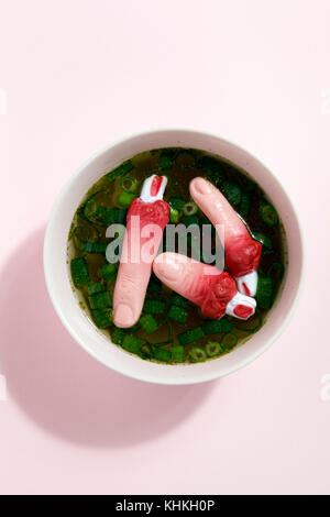 Les doigts d'un bouillon de viande avec des oignons verts flottant à la surface de la soupe dans un bol rose. Couleur du dégradé. Minime et la photographie originale. Banque D'Images
