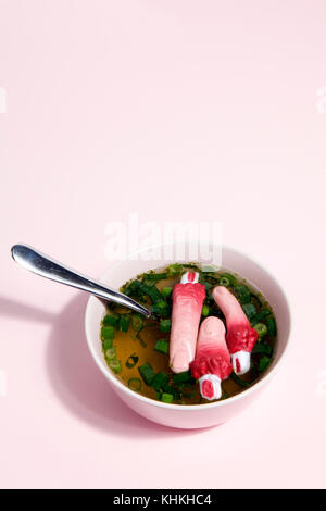 Les doigts d'un bouillon de viande avec des oignons verts flottant à la surface de la soupe ainc une cuillère n un bol rose couleur du dégradé.. minimal et décalé la photographie. Banque D'Images