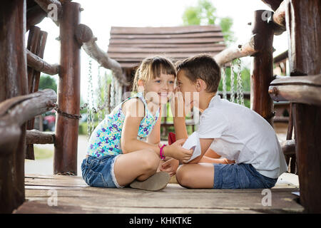 Deux frères de race blanche sittign heureux dans une maison en bois en plein air, sur la tenue d'un jour d'été, bateaux de papier dans les mains, boy whispering a secret en rif Banque D'Images