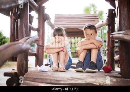 Deux jeunes enfants de race blanche assis à côté de l'autre avec les genoux pliés dans une maison en bois, l'extérieur dès les beaux jours d'été. Ils ont l'air innocent Banque D'Images