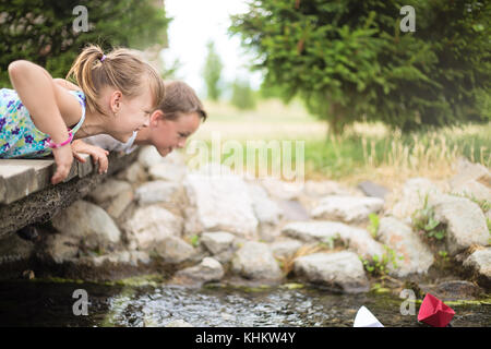 Deux jeunes enfants caucasiens allongé sur un petit pont en bois au-dessus du petit ruisseau, regarder les bateaux en papier flottant sur un plan d'eau Banque D'Images