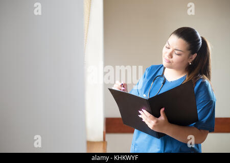 Young hispanic female doctor l'analyse d'un cas clinique, à la recherche dans un dossier qu'elle tient dans ses mains. femme porte un uniforme bleu, debout je Banque D'Images