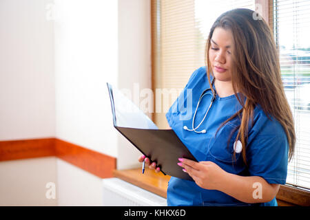 Jeune femme médecin sérieux de l'analyse d'un cas clinique, à la recherche dans un dossier qu'elle tient dans ses mains. femme porte un uniforme bleu, debout dans Banque D'Images